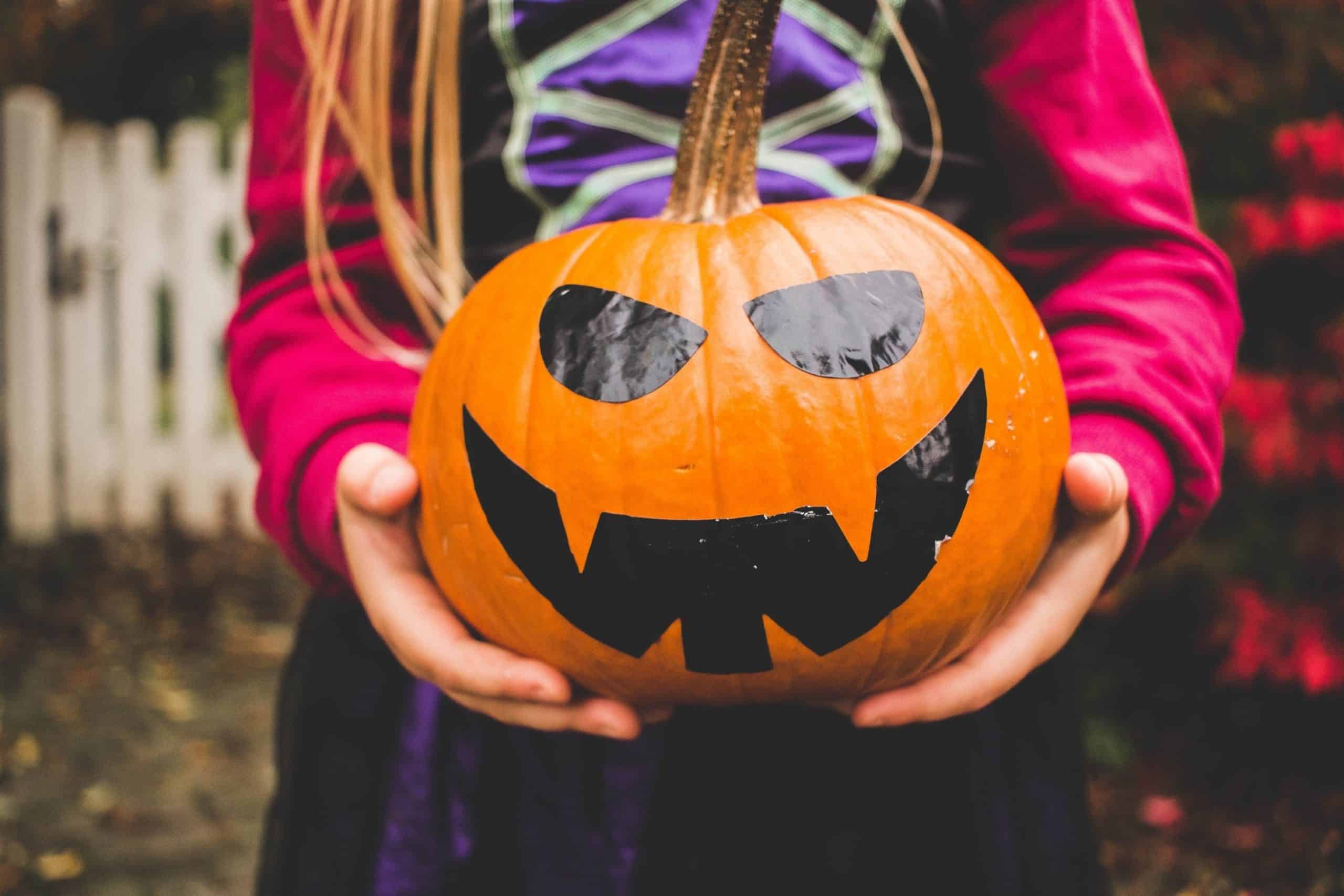 Little Girl Holding Decorated Large Pumpkin Ready For Halloween