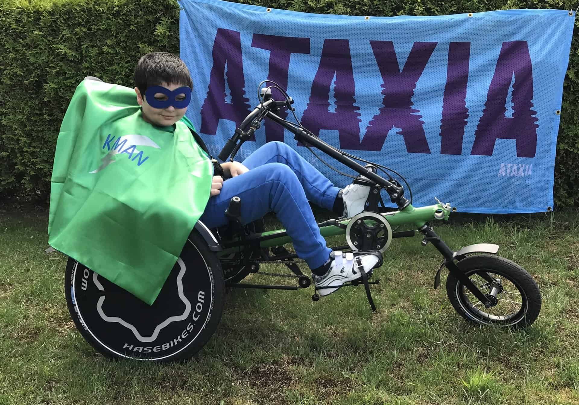 Kieran Hankin, with Ataxia UK banner and in superhero outfit